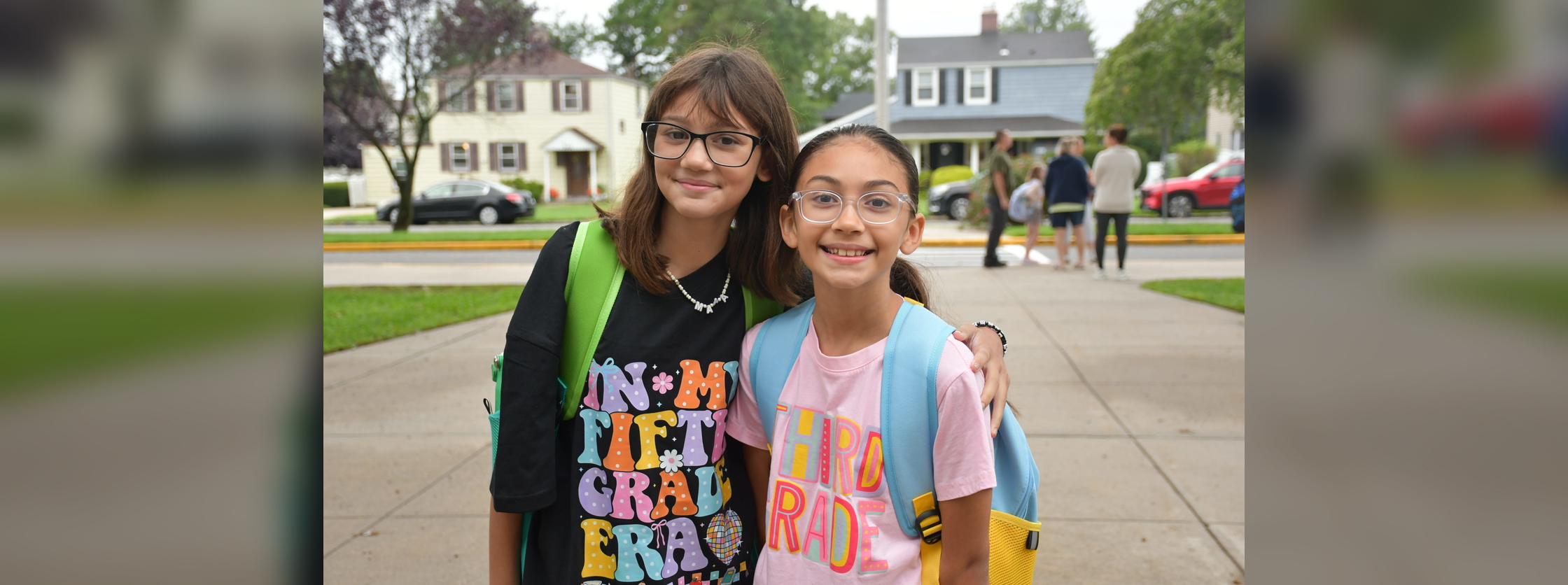 Two happy girls posing together outside in colorful back-to-school outfits with backpacks.