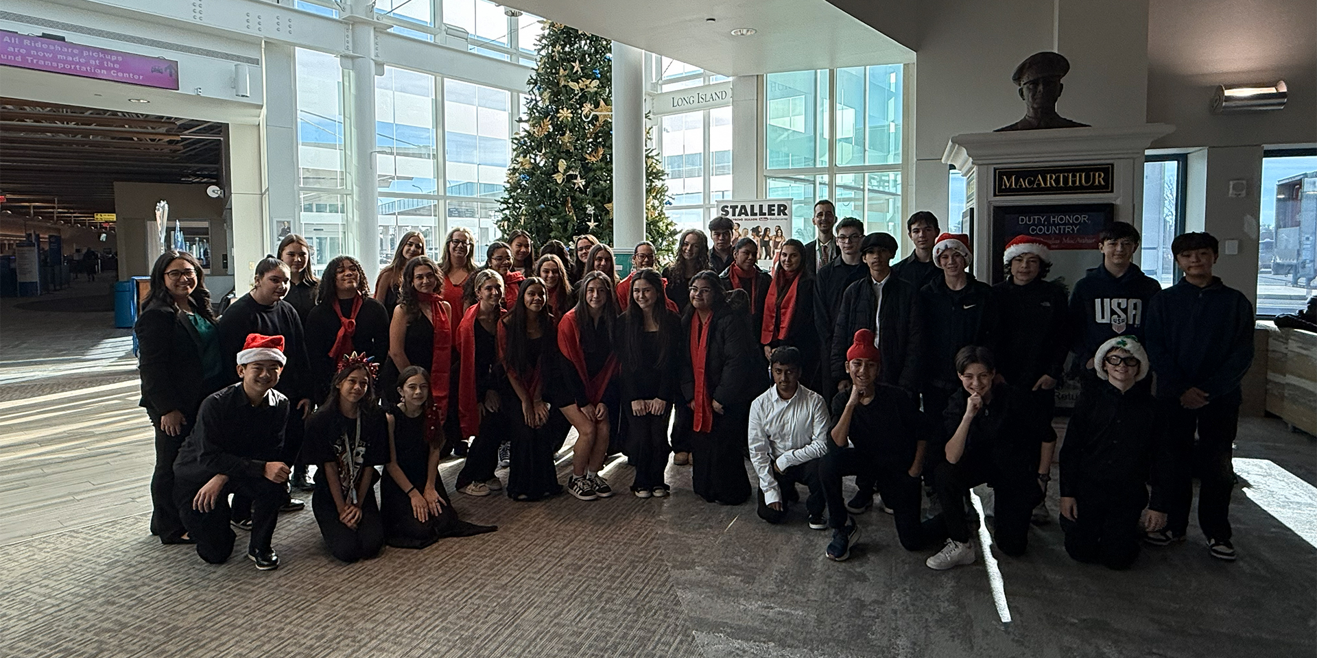 A large group of people, some in holiday attire, pose in an airport terminal. 
