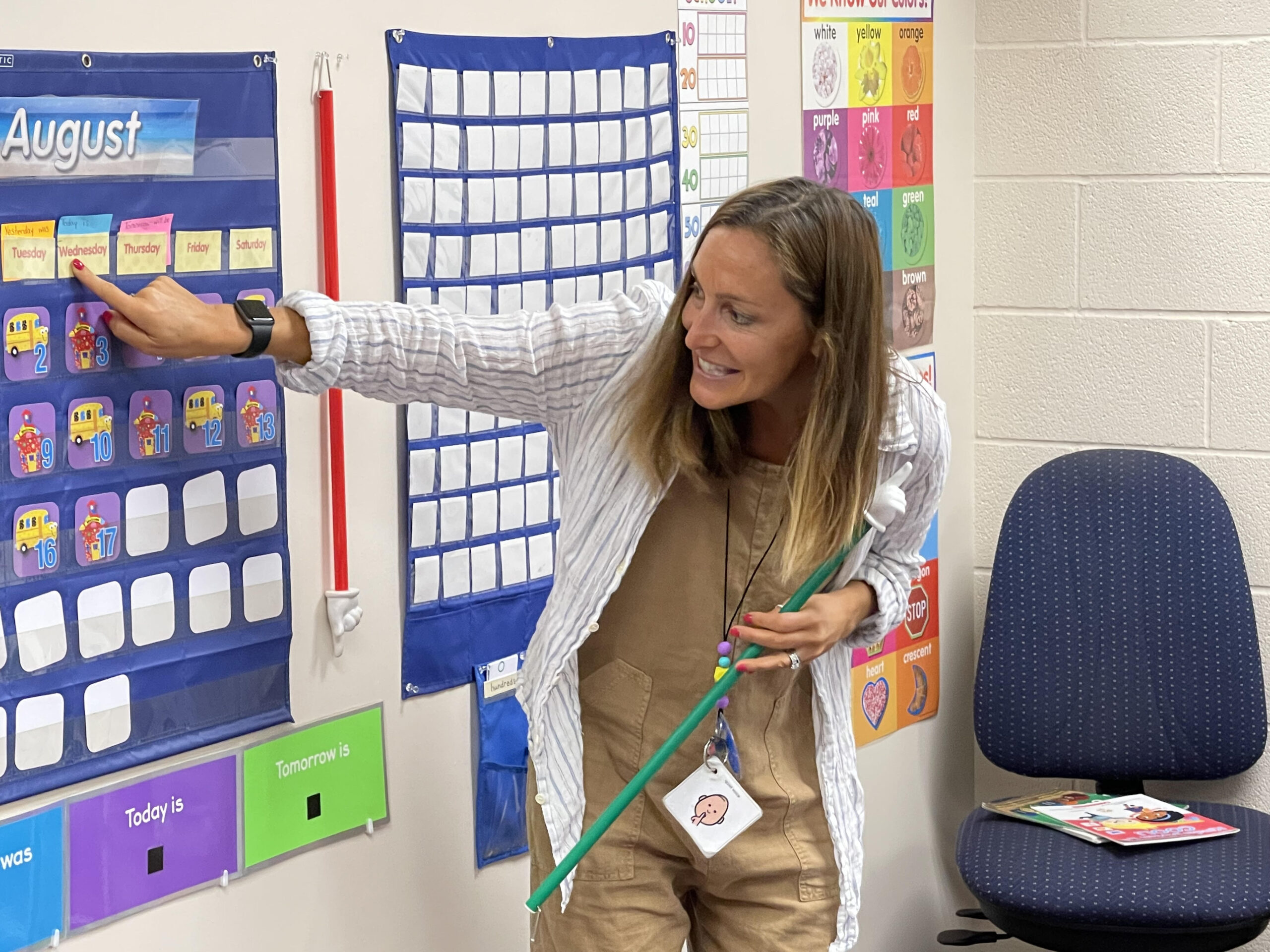 A woman pointing to a calendar on a wall, indicating a specific date or event.