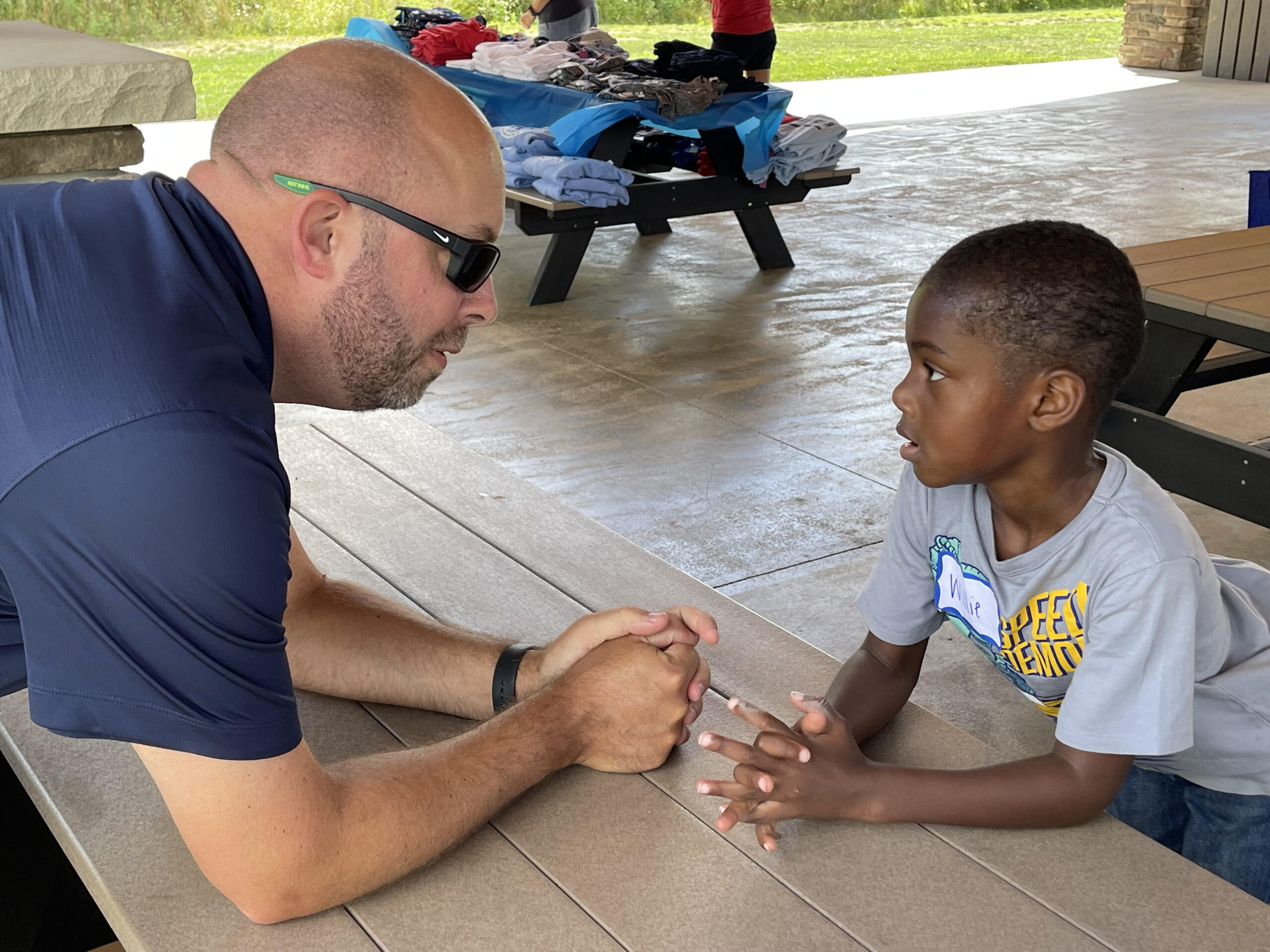 An adult male and a child sitting together at a picnic table outdoors.