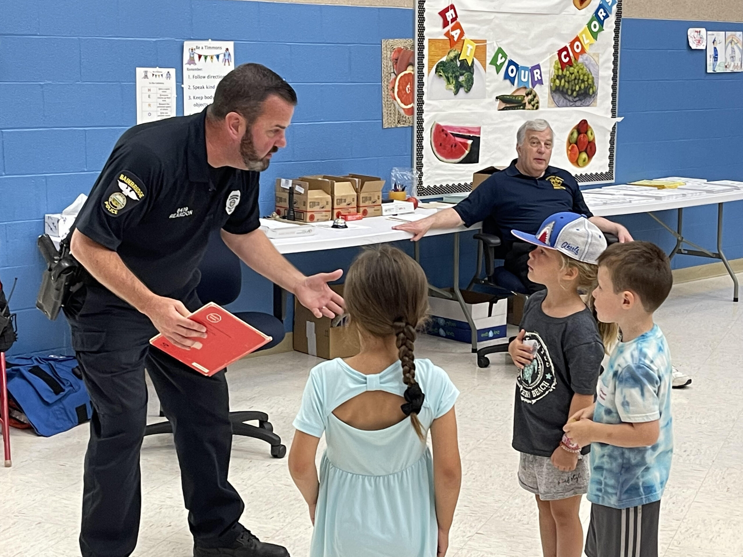 A police officer engaging with children in a classroom setting, discussing safety and community awareness.