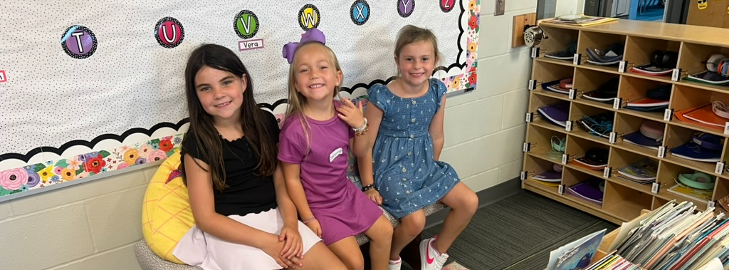 three students sitting together on a bench in the classroom reading nook