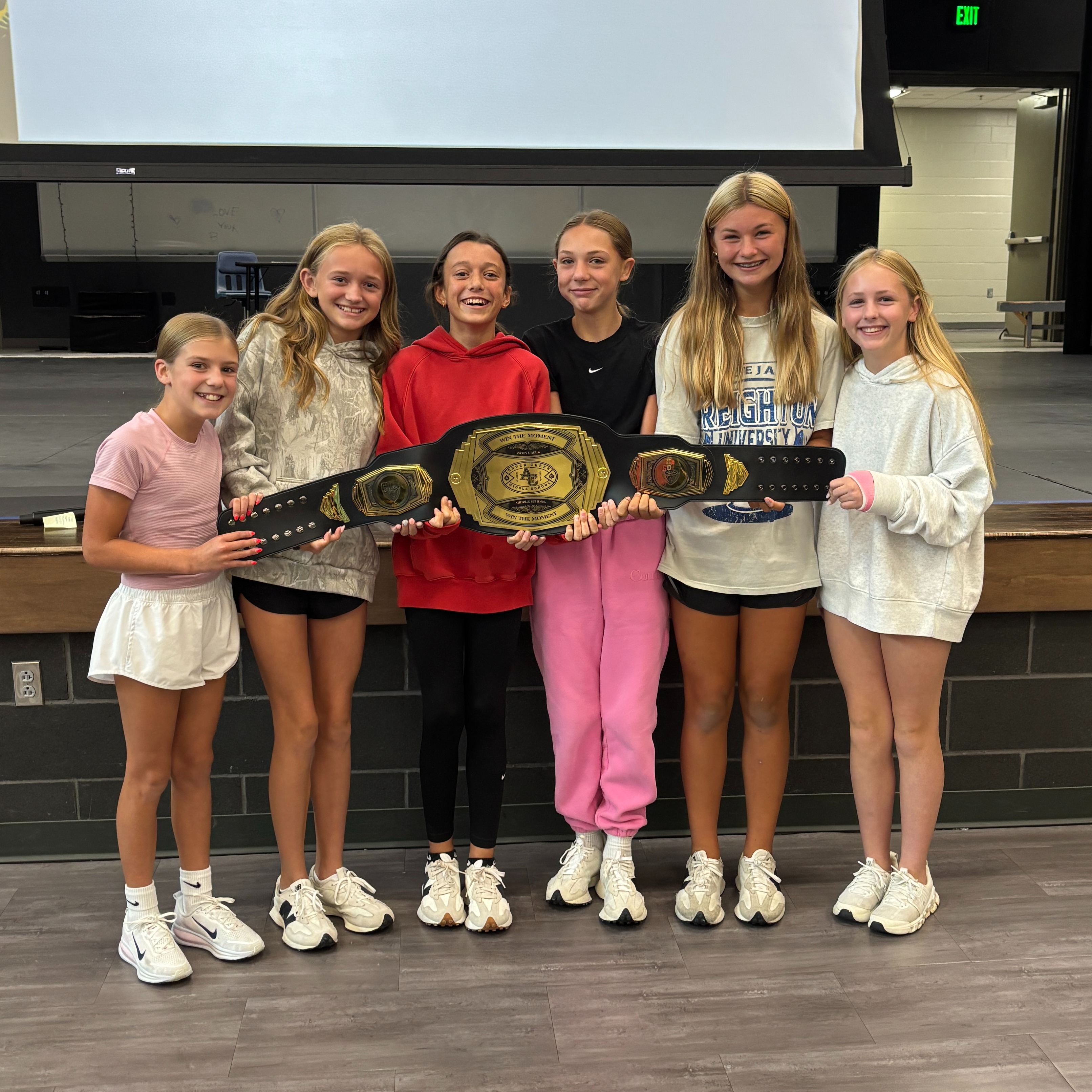 girls standing in front of stage holding belt for "Win the Moment"