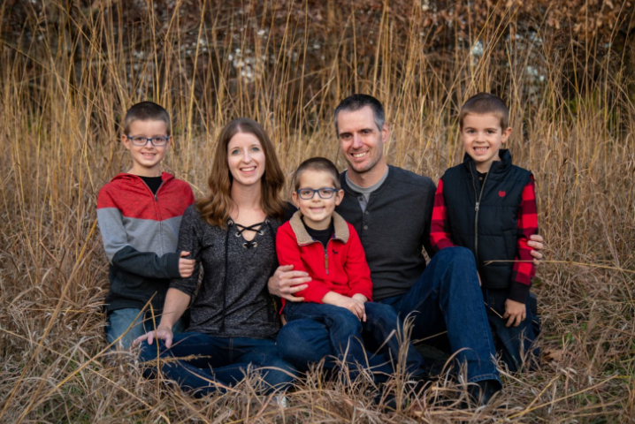 Photo of couple with three children sitting in a field of tall grass posing for the camera