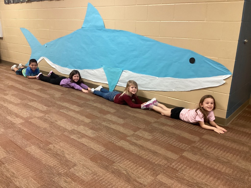 students laying on the floor in the hallway under a large paper whale on the wall