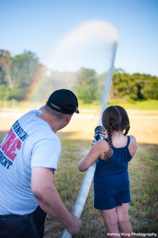 Firefighter showing girl how to use fire hose