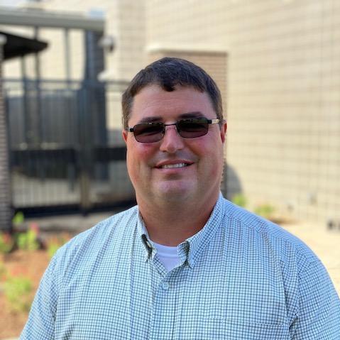 A man in sunglasses and a shirt standing outdoors.