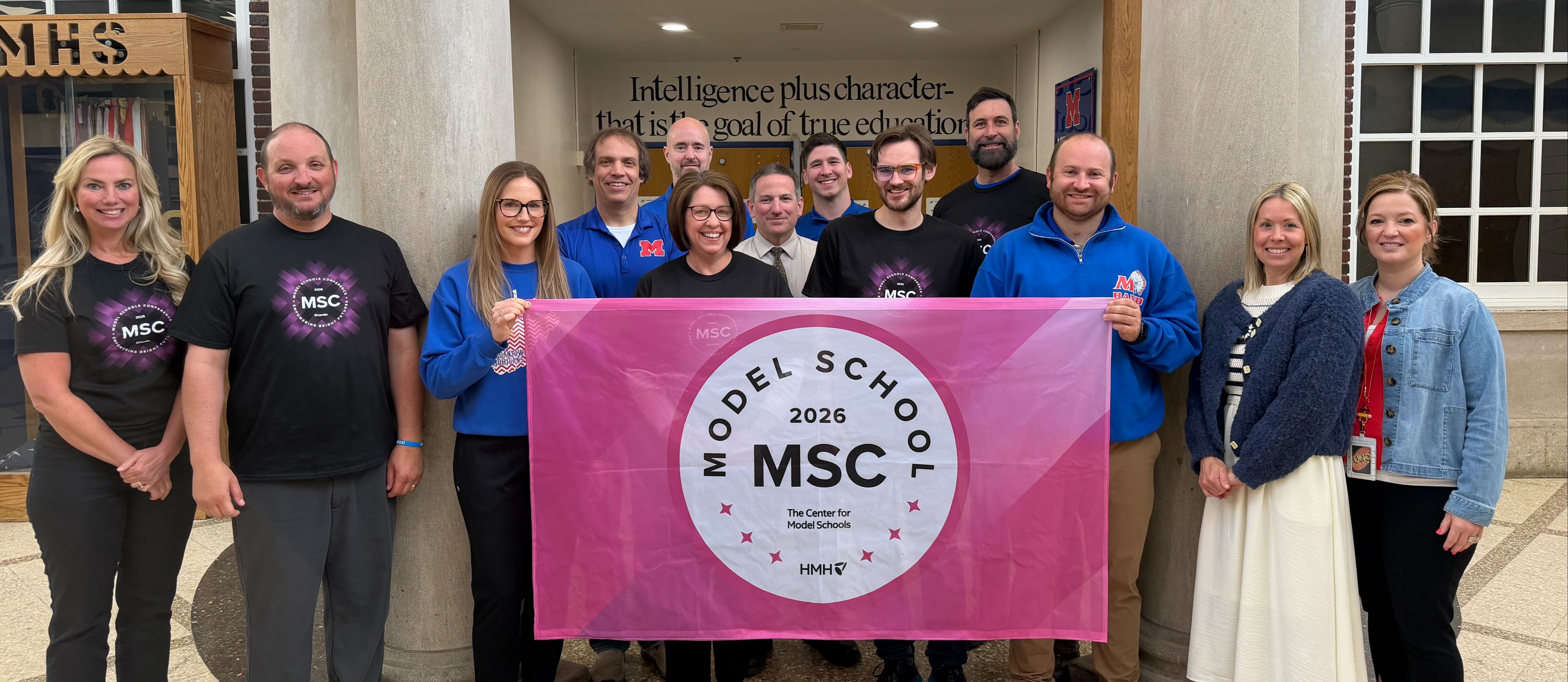Group of people standing around with a flag that says Model School 2026 MSC