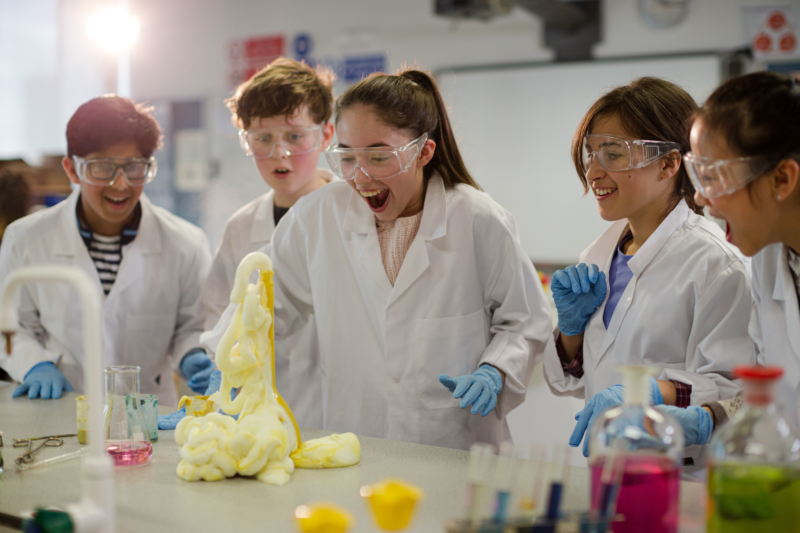 middle school students in lab coats doing an experiment that erupts in a yellow substance.