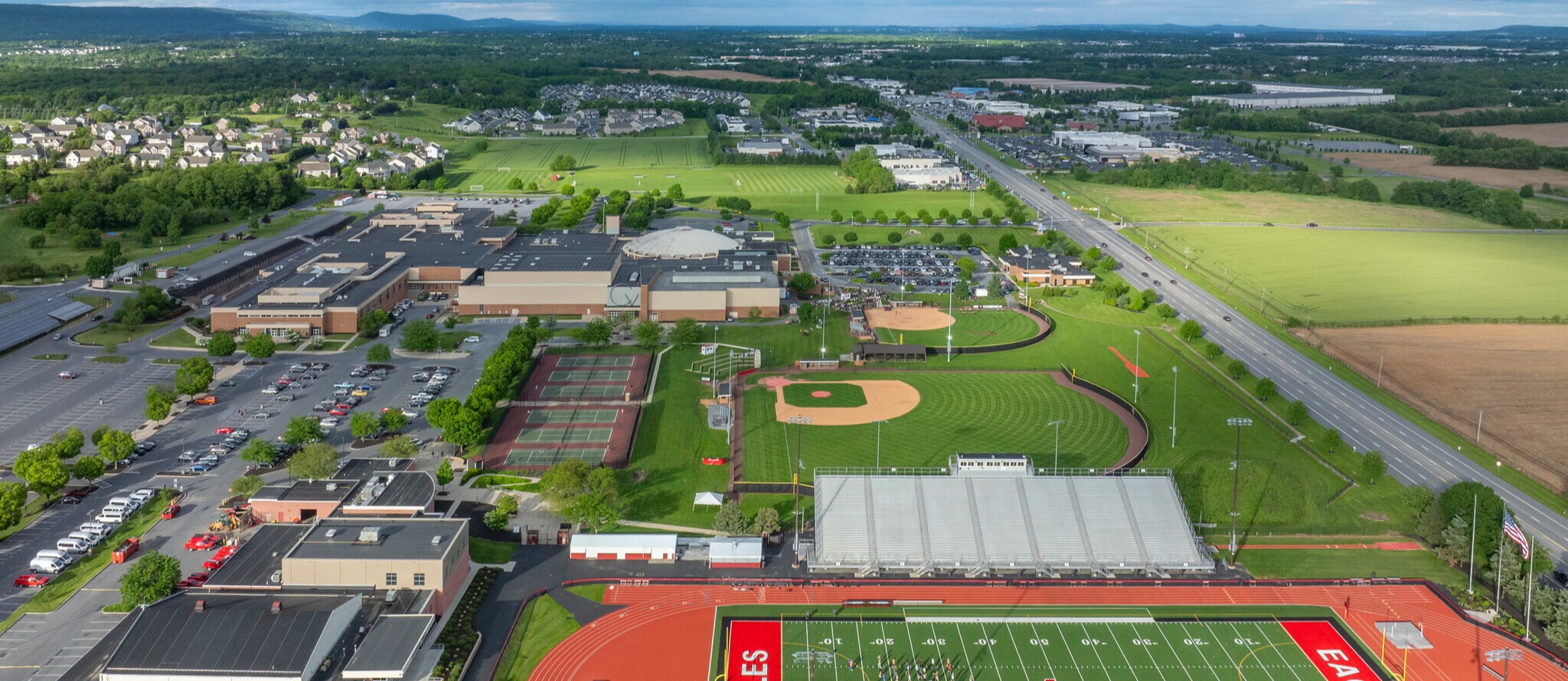 Aerial view of the school campus showing academic buildings, athletic facilities, parking areas, and surrounding community landscape.