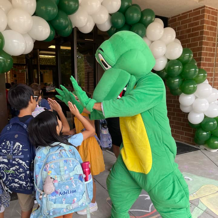 Photo of a gator giving a high five to two students.