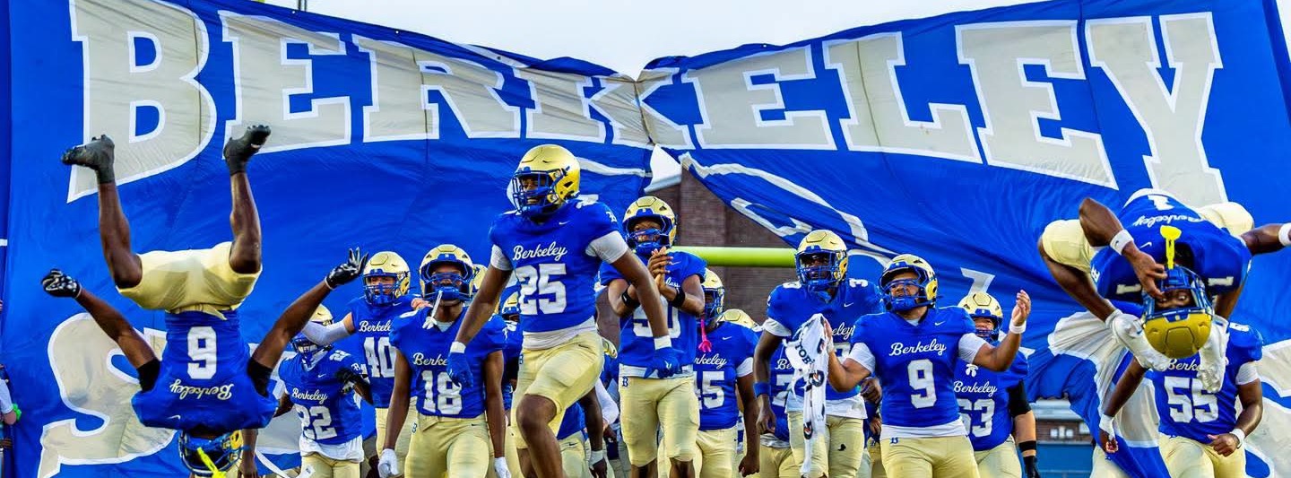 Berkeley football team in blue uniforms and gold helmets running onto a field, with a blue banner in the background.