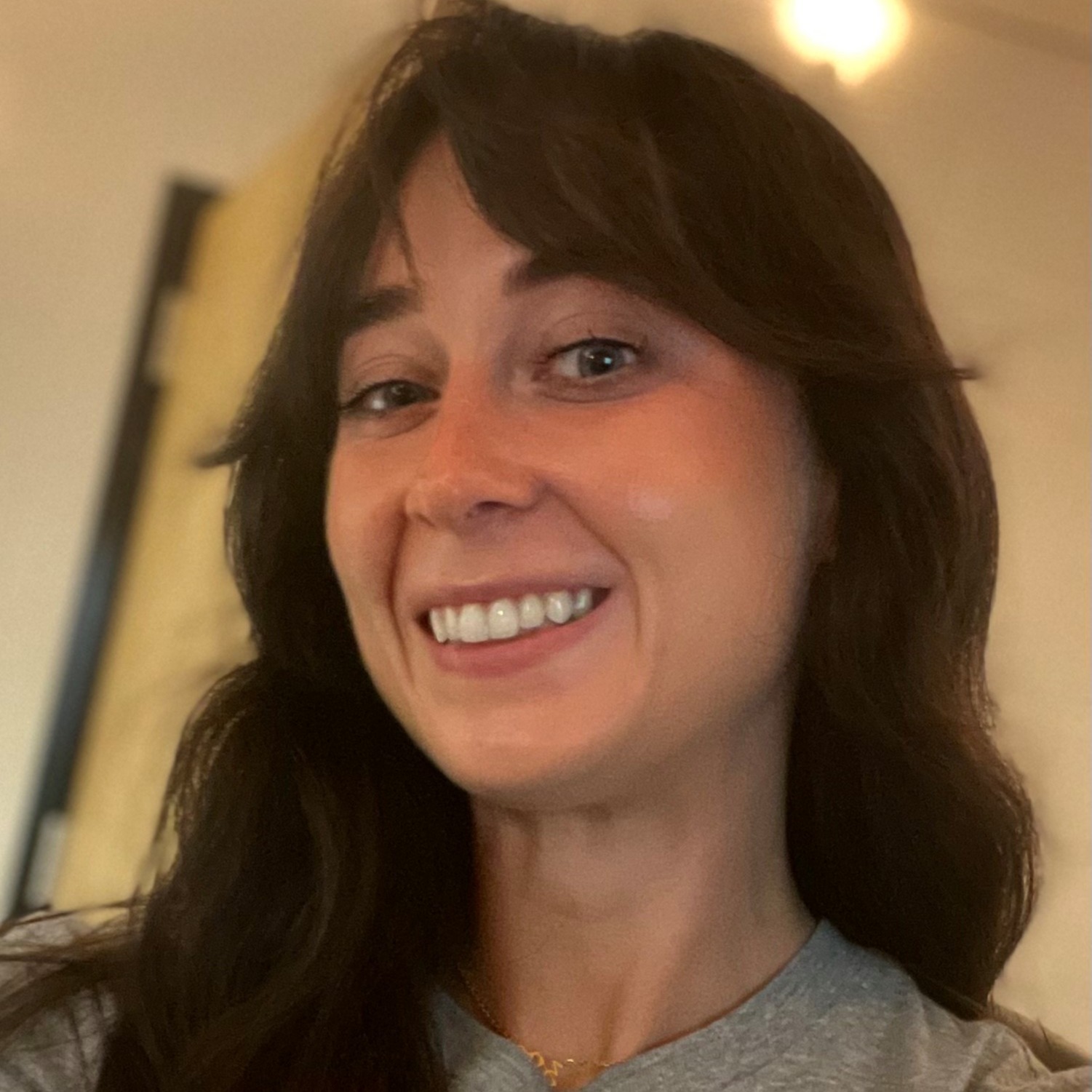 Woman with long brown hair and a gray t-shirt, smiling and looking at the camera.
