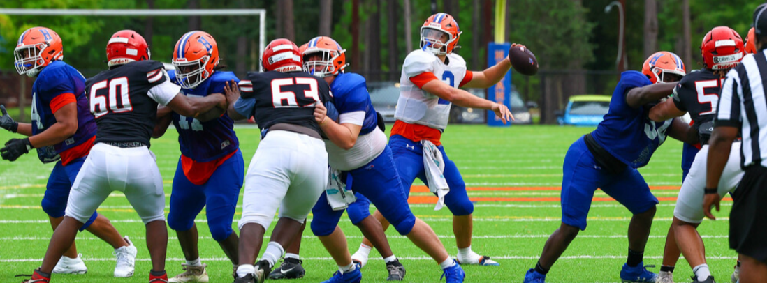 Football players in blue and white uniforms on a field, one quarterback preparing to throw, others engaging in play.