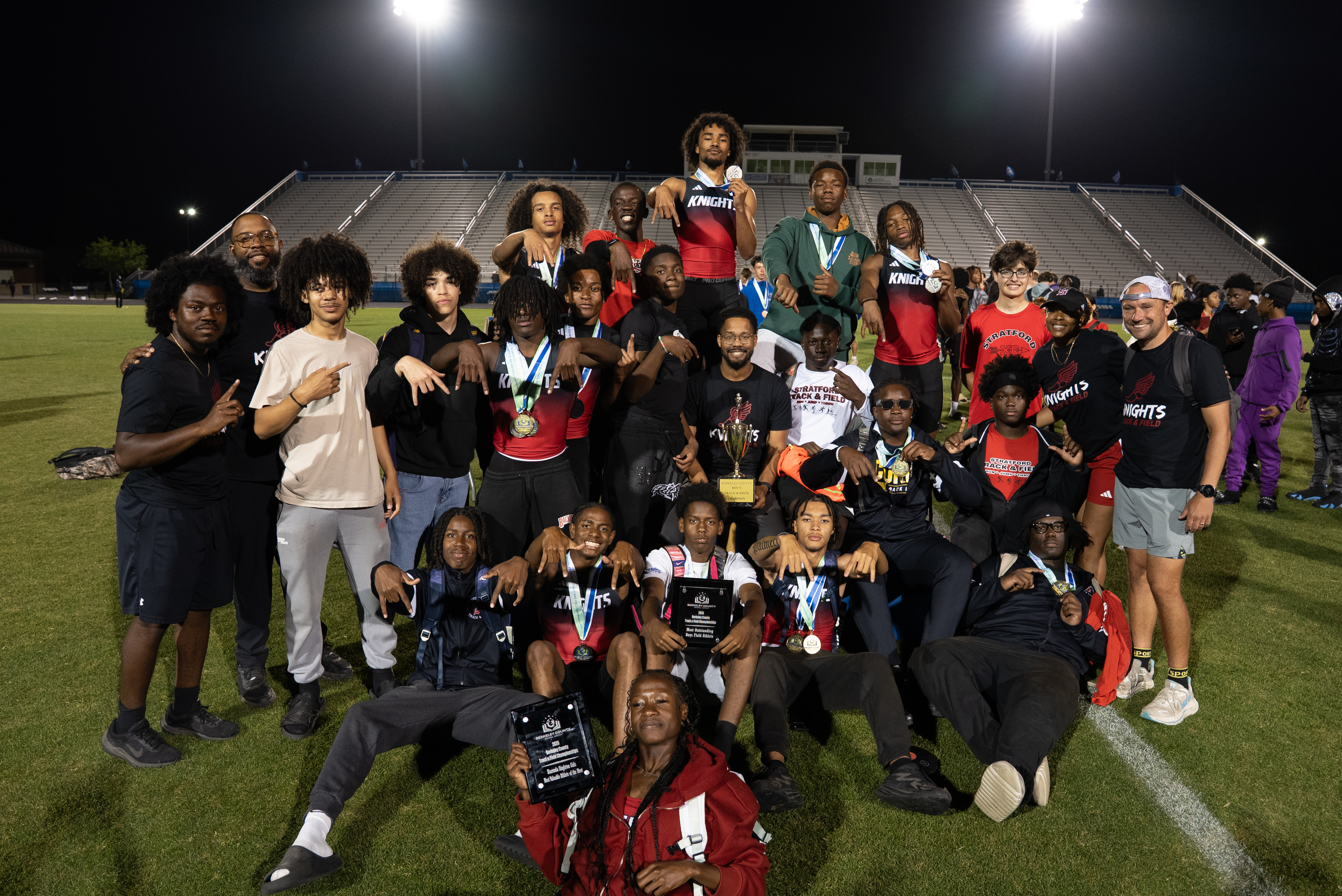 A group of people in sports gear, some holding medals, pose for a photo on a grassy field.