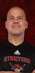 A man with a smile, wearing a black Adidas shirt. The shirt has "Stratford" written in red on the front.