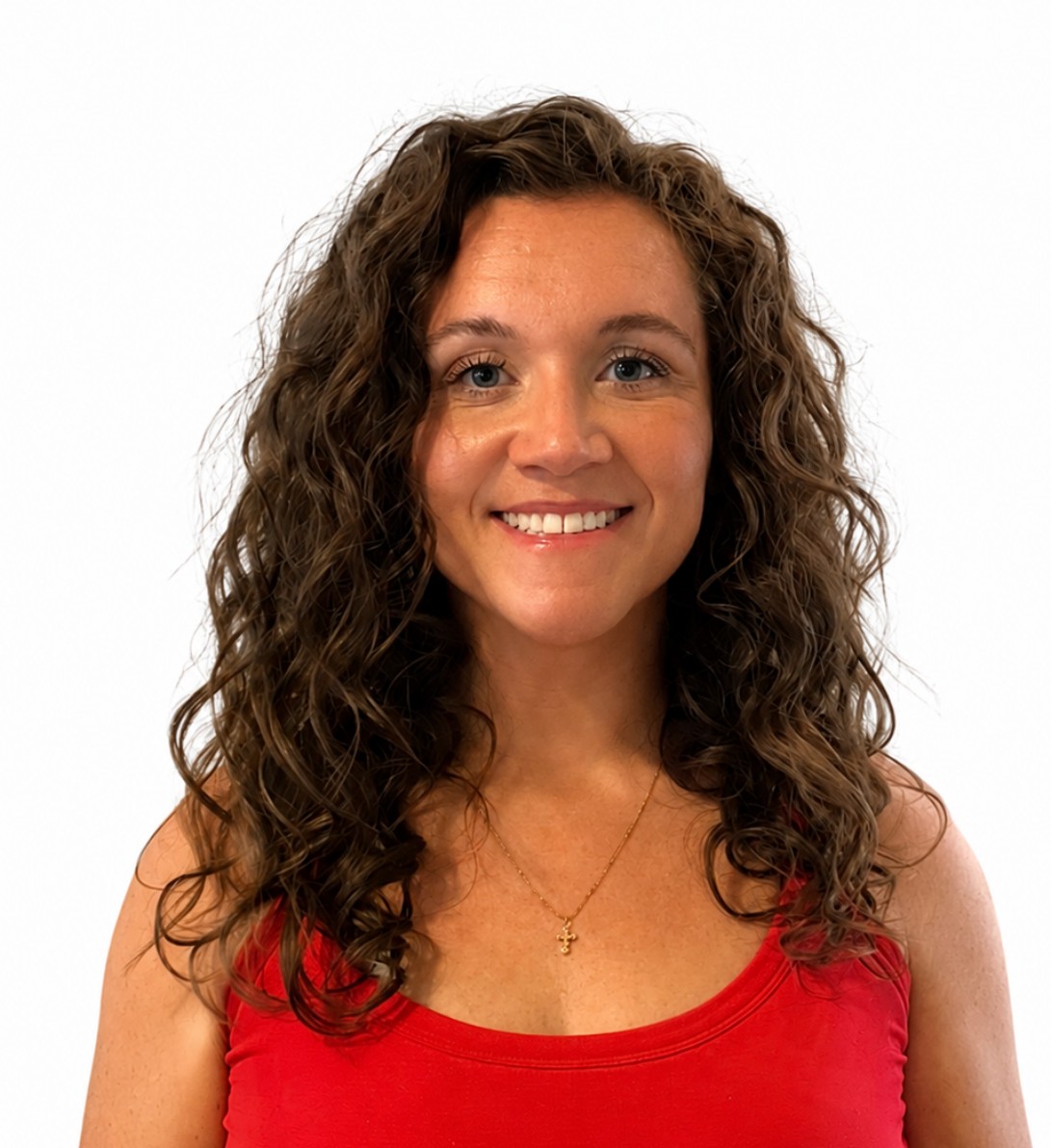 A woman with curly hair smiles, wearing a red sleeveless top and a gold necklace. She stands against a plain white background.