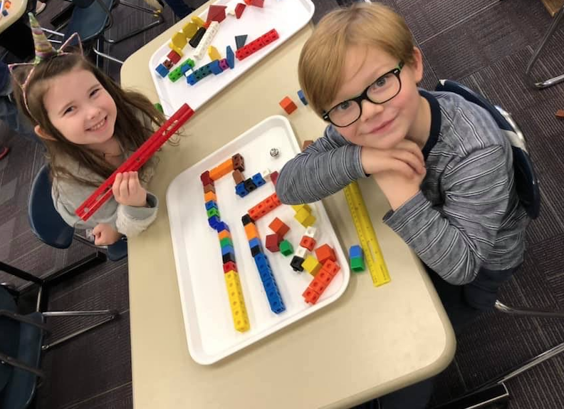 Two kids playing with different legos and cubes to make a form