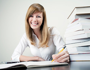 A blonde woman smiling next to a stack of books.