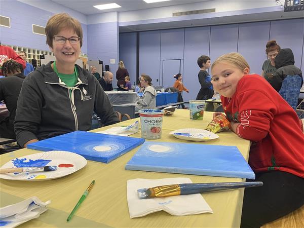 a teacher and student are seated at a table with art canvases and paintbrushes