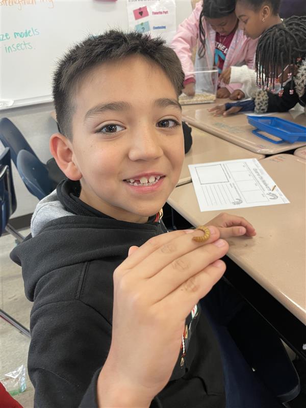 a student holds a worm on the back of his hand and smiles at the camera