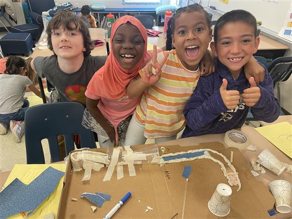 four students smile and give peace signs and thumbs up. 