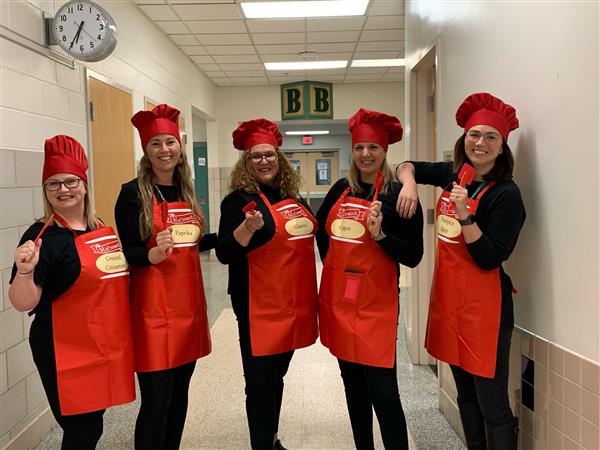 5 teachers pose together in a hallway wearing red chef hats and matching aprons