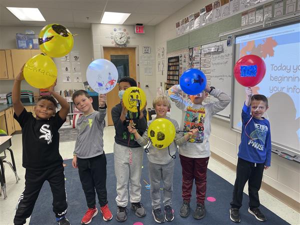 six students hold up balloons they've drawn on