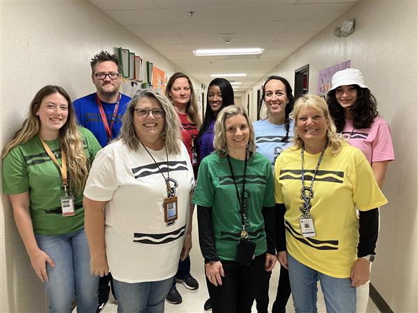 9 teachers pose in the hallway wearing matching crayon inspired t-shirts