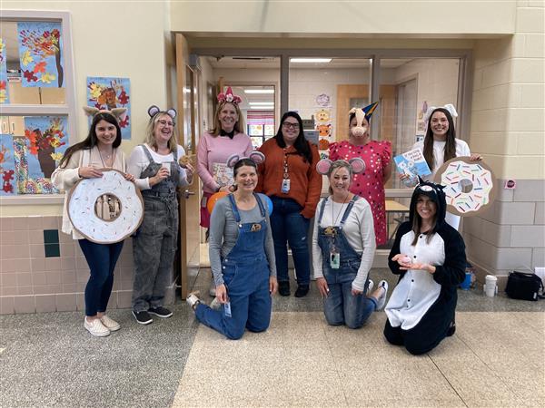 teachers pose in a hallway dressed as donuts, unicorns, and mice 