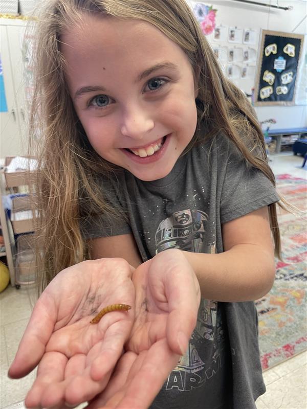 a student holds up a worm and smiles