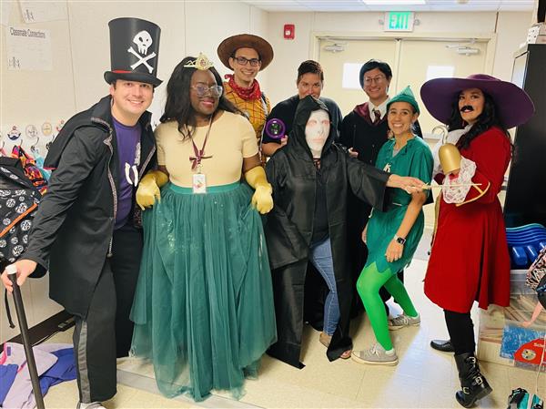 eight teachers pose in their Halloween costumes - a skeleton, a princess, Woody from Toy Story, Voldemort and Harry Potter, Peter Pan and Captain Hook