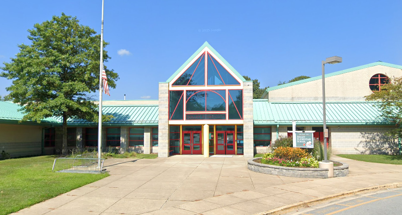 Building with green roof and glass windows. Red double doors and flagpole in front. Green lawn and trees.