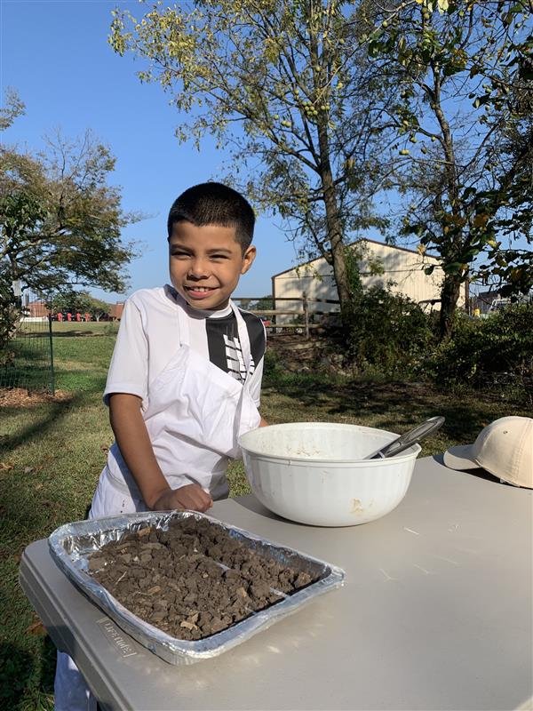 A young boy happily stands before a table, grinning, as he gazes at a bowl of food placed on it.
