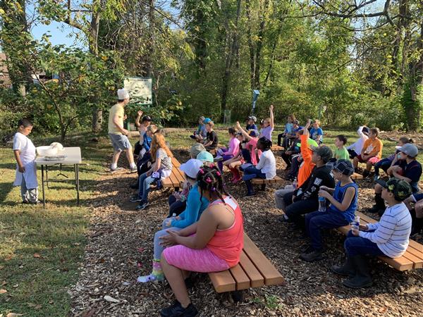 A woman teaches a group of children about nature as they sit around a table, engaged in learning.
