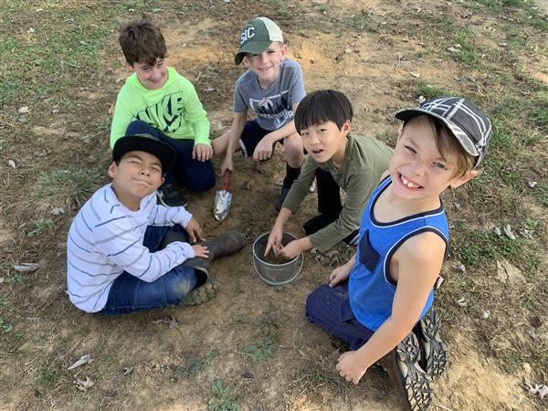 Four boys sitting on the ground, one holding a bucket.