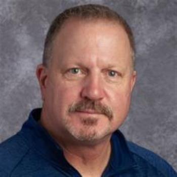 A man with a mustache wearing a blue shirt.