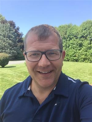 A man in glasses and a polo shirt taking a selfie.