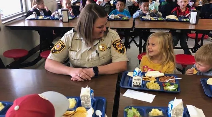 kid looking at an officer at a lunch table, they're smiling at each other