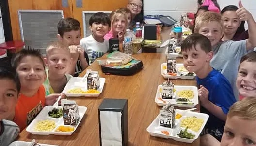 kids happy on the cafeteria seated with their lunch trays, about to eat