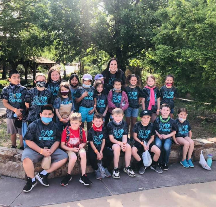 large group of students outdoors with custom shirts smiling at the camera