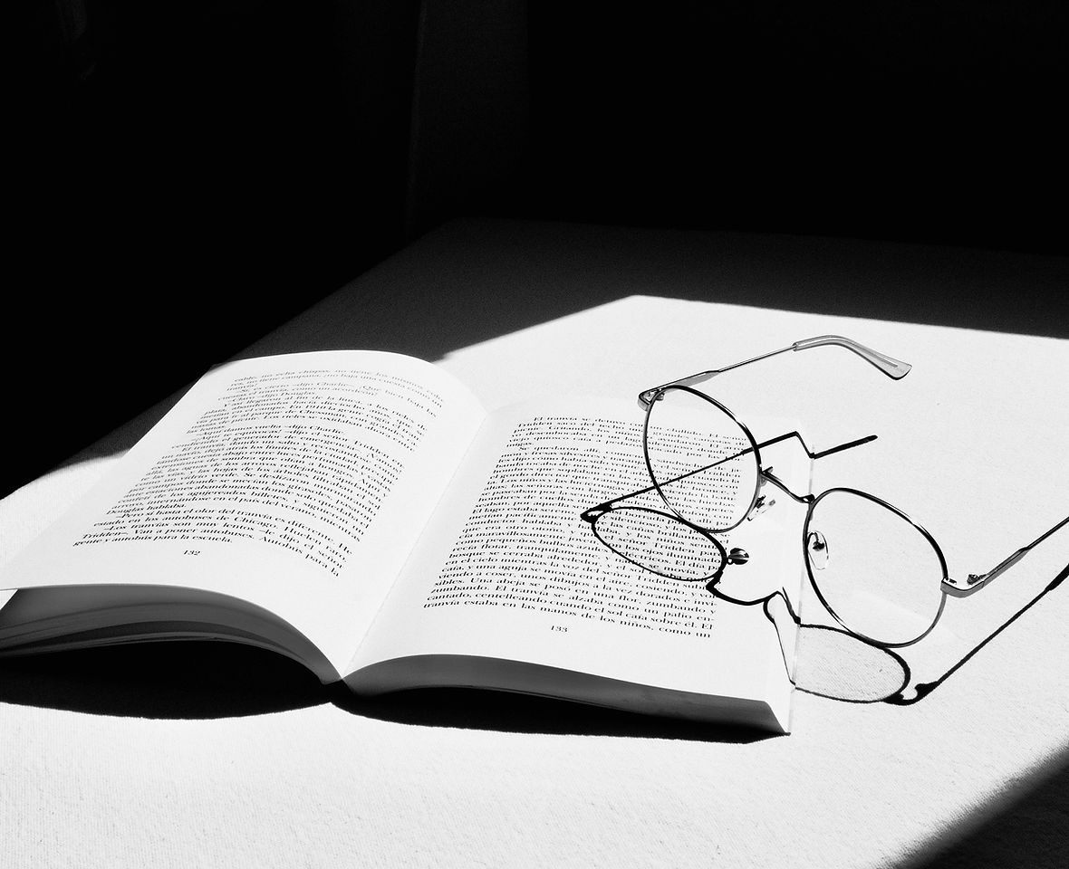 picture of a book open and glasses on top of them, the picture is black and white