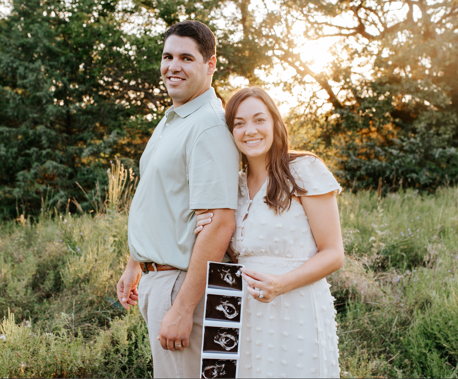 Photo of a couple in a field holding an image of ultrasound images of baby