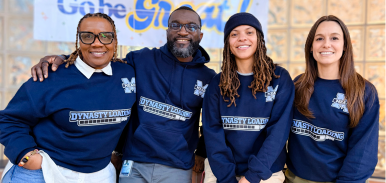 Four adults in blue sweatshirts with logos stand before a banner with the words "Gobe Great."