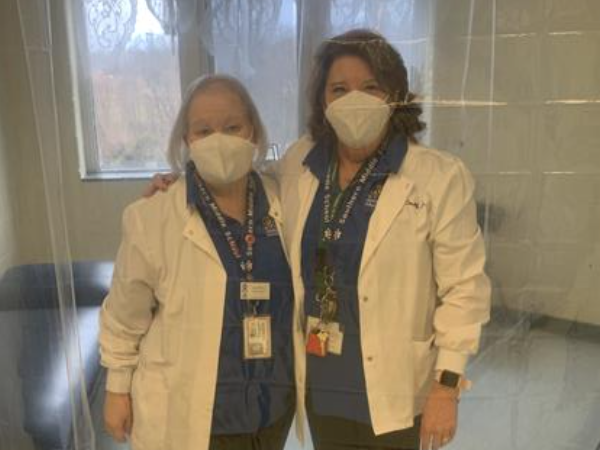 Two  staff members in white coats and masks, posing for a photo