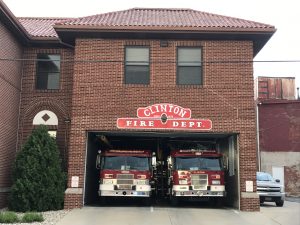 The image depicts the Clinton Fire Department, a brick building housing two red fire trucks