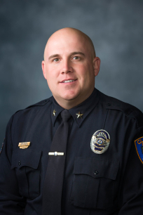 A person in a dark blue police uniform stands against a dark background