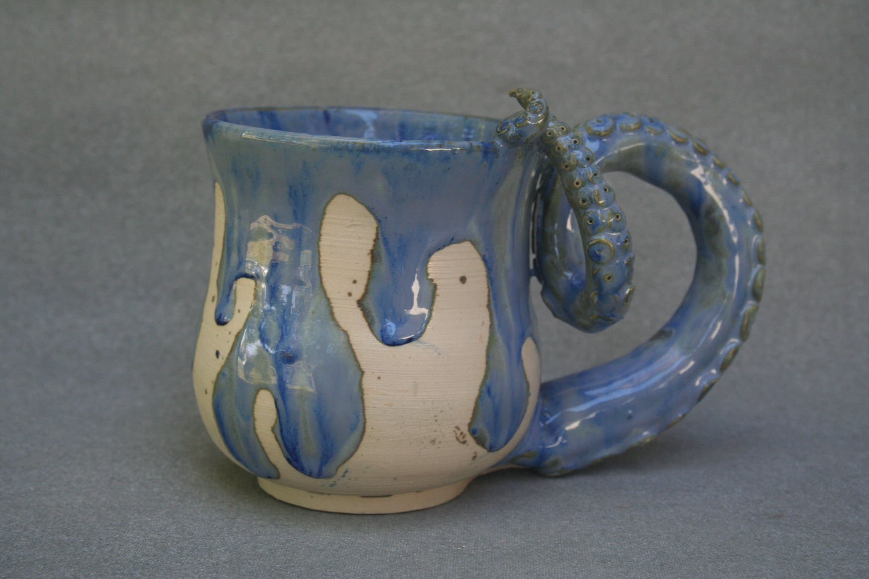 A photo of a handmade ceramic mug painted in white and blue, the handle of it resembling an octopus tentacle