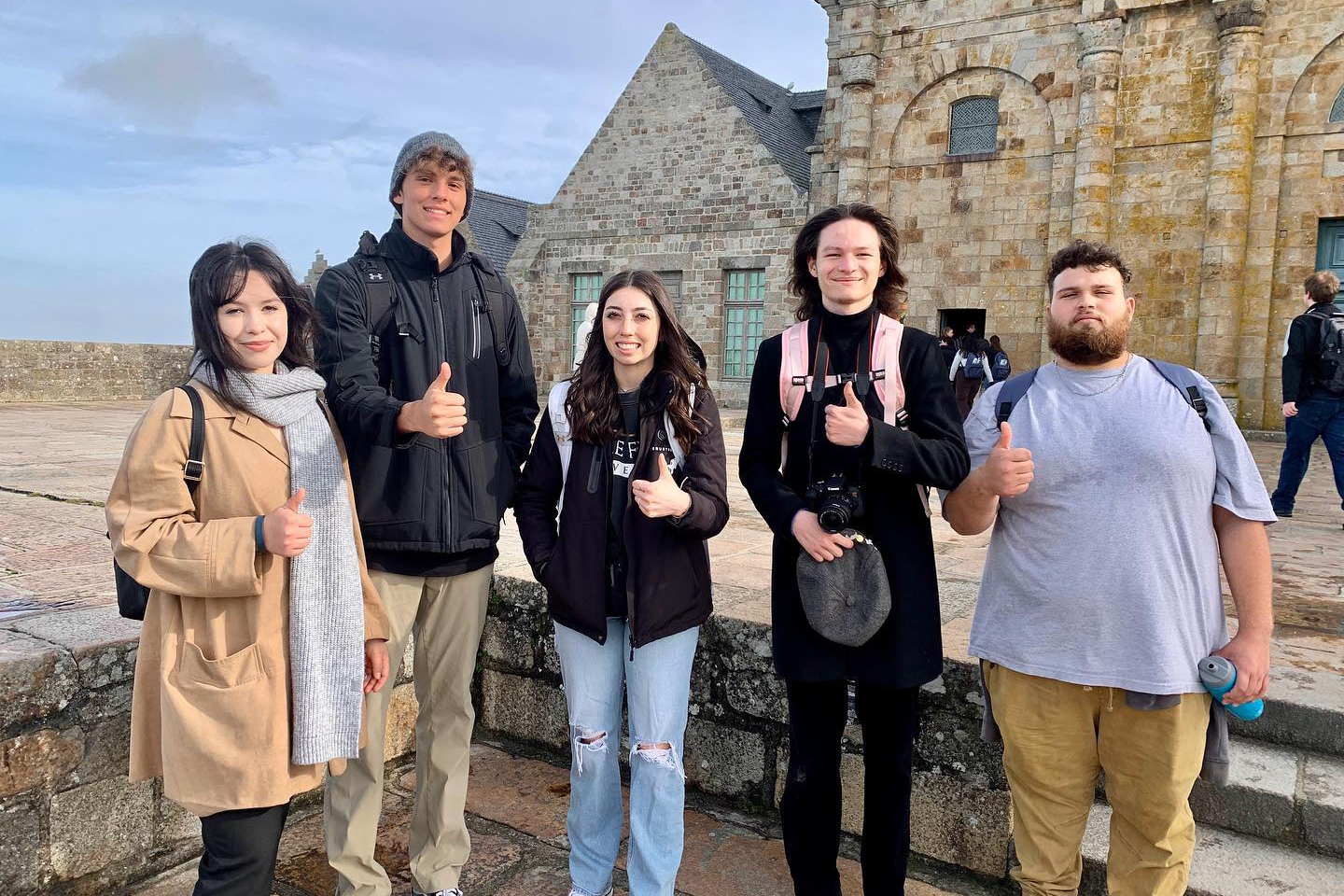 A group of 5 high school students giving a thumbs up on their trip to France.