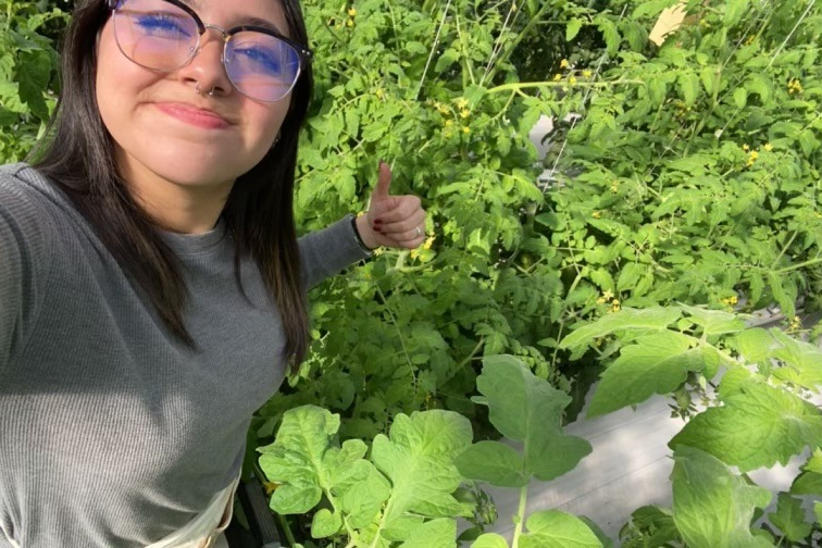  A person giving a thumbs up in a garden with lush green plants.